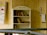 A bookshelf labeled 'La Vereda Literaria' filled with various books, located outdoors against a wooden wall. Nearby, a handmade signs with colorful drawings and text are attached to the wall.