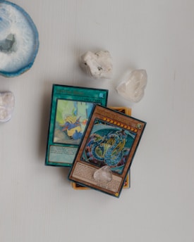 Several collectible cards, including a Spell card titled 'Crystal Bond' and a Dragon card, lie on a light surface. Nearby, there are a few polished crystals and a large, round blue geode add a natural element to the composition.