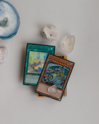 Several collectible cards, including a Spell card titled 'Crystal Bond' and a Dragon card, lie on a light surface. Nearby, there are a few polished crystals and a large, round blue geode add a natural element to the composition.