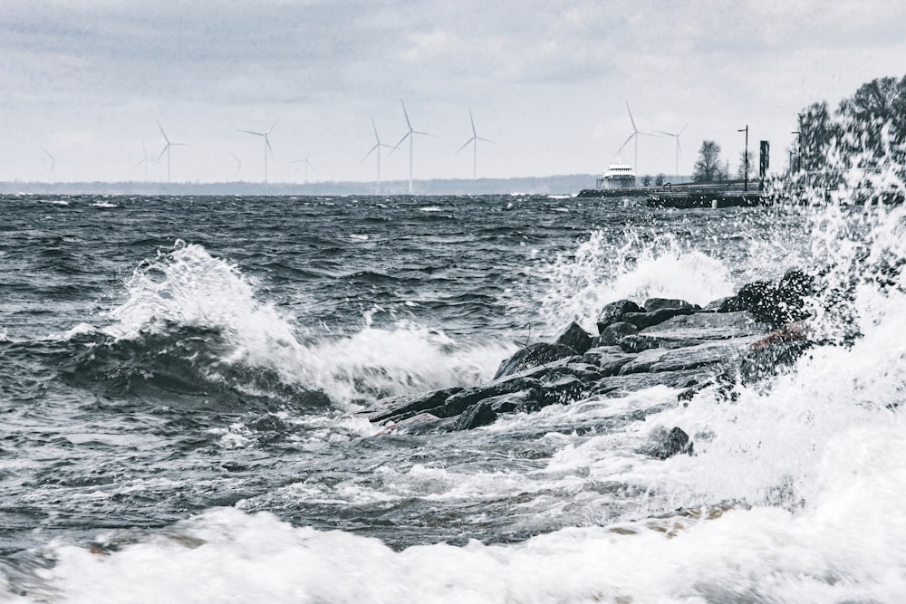 waves crashing on a rocky shore with wind mills in the background