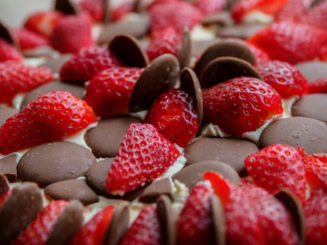 Freshly sliced strawberries are generously spread over layers of chocolate discs, creating an appealing contrast between the vibrant red of the fruit and the rich brown of the chocolate. The strawberries are embedded in a creamy base, adding to the texture and indulgence of the arrangement.