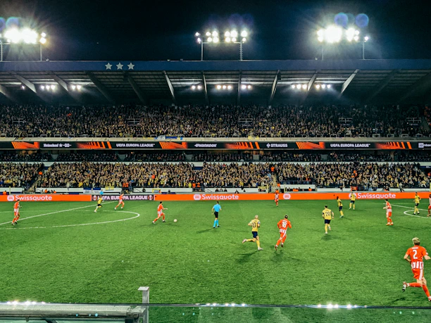 A vibrant stadium filled with cheering fans under bright floodlights during a soccer match.