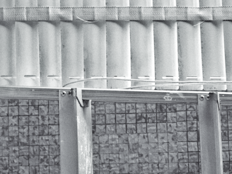 A grayscale image depicting the upper part of a corrugated metal sheet structure, with a patterned band running horizontally across the top portion. The lower part consists of a grid-like design with a mosaic pattern. The combination of textures and patterns suggests an industrial or architectural theme.