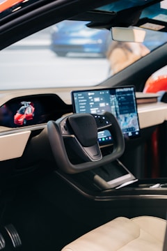 The interior of a modern car featuring a large digital dashboard and a sleek steering wheel design. A navigation screen and various controls are visible, highlighting advanced technology. The environment looks polished and futuristic.