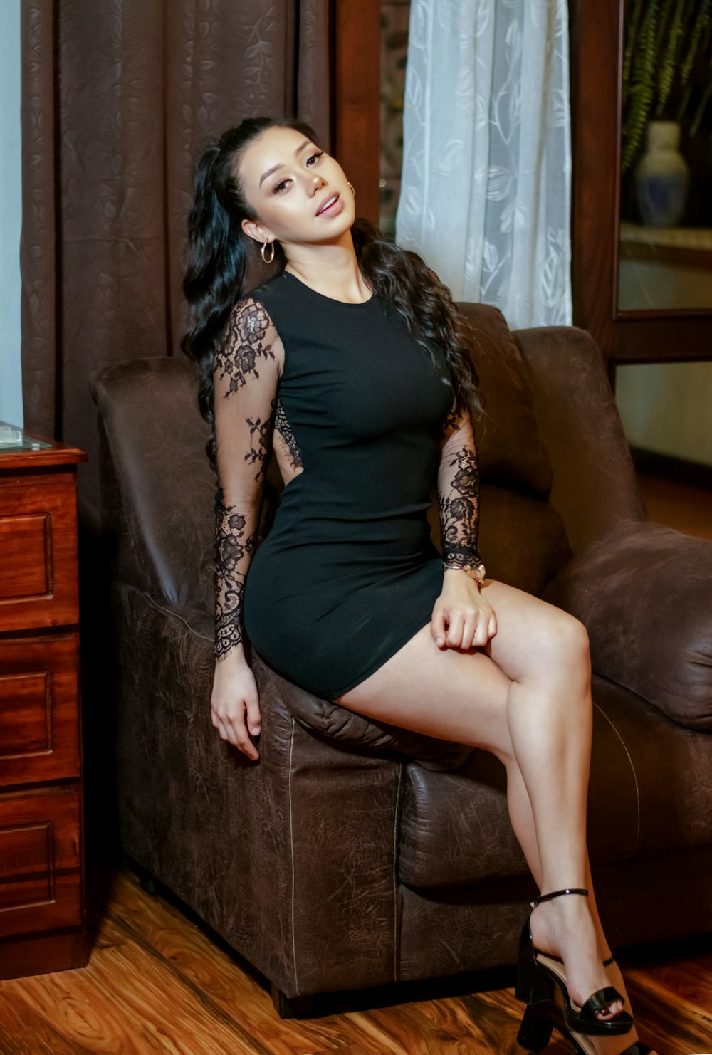 a woman in a black dress sitting on a brown couch