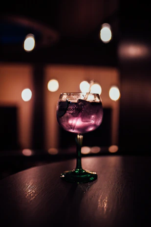 Close-up of a sophisticated cocktail glass reflecting ambient purple and gold lighting.