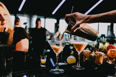 Close-up of a bartender pouring cocktails at the open bar with happy guests around.