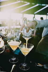 a bartender pours a martini into two martini glasses