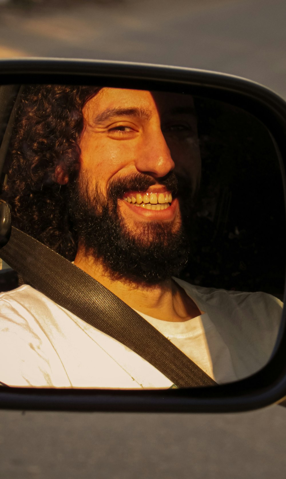 a man with long hair and a beard smiling in a car mirror