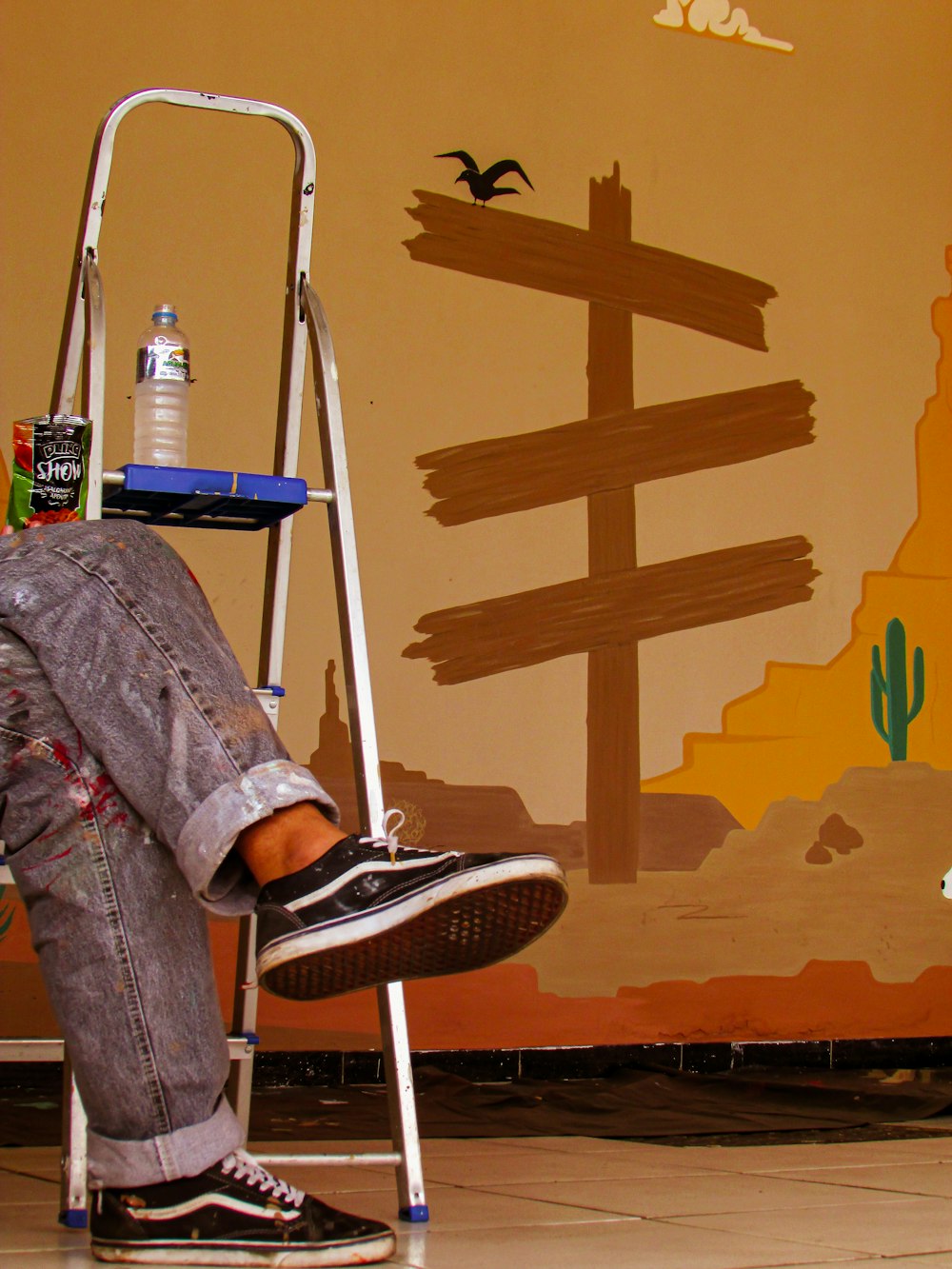 a man sitting on a step ladder painting a mural