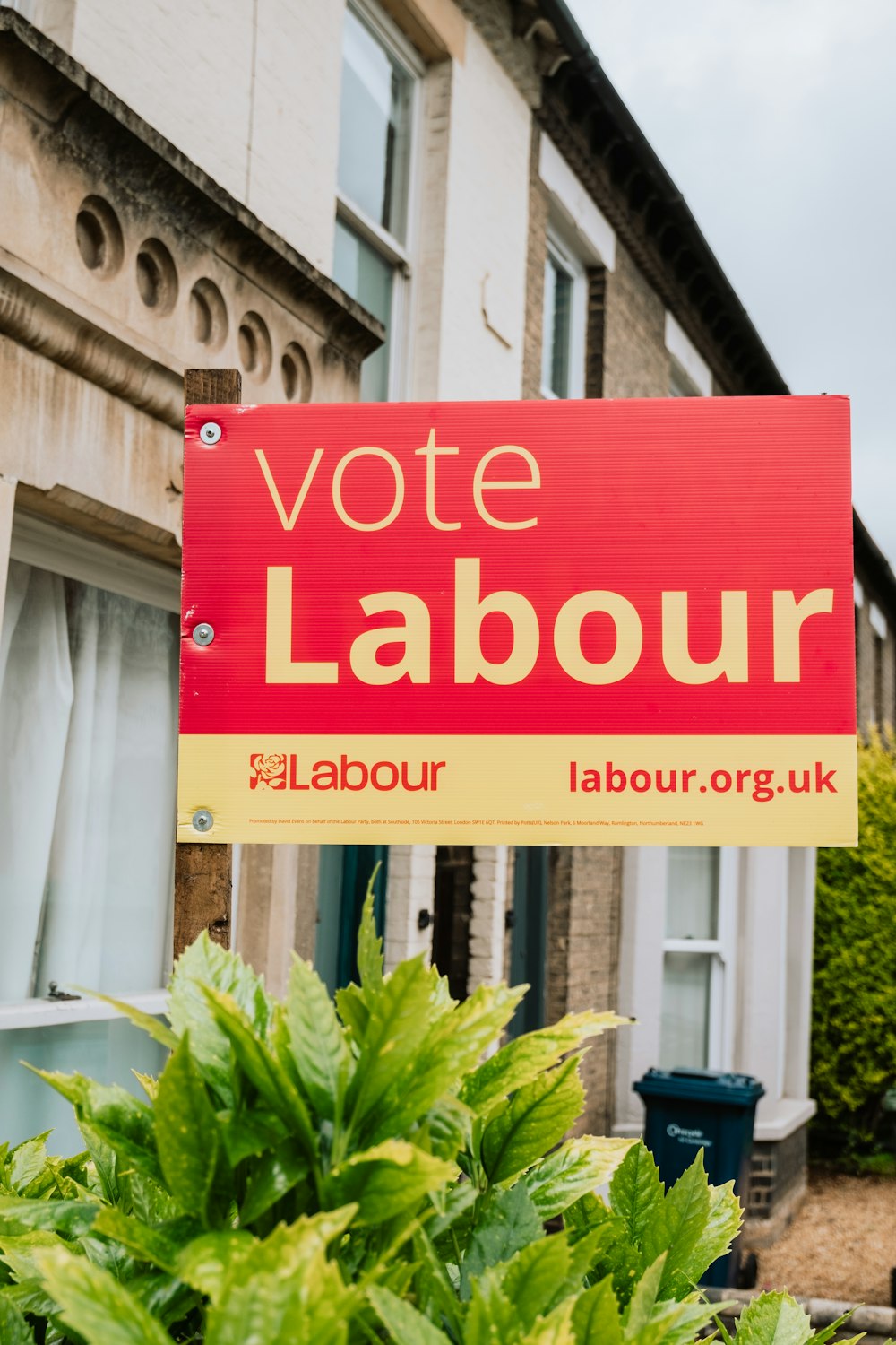 a red and yellow vote labour sign in front of a house