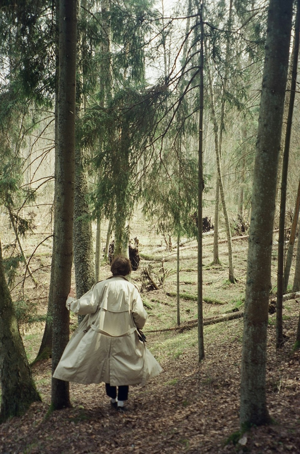 a woman in a white coat walking through a forest