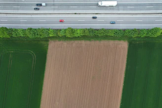 Aerial view of multiple trucks moving along a highway surrounded by green fields.