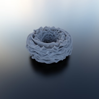 A complex, abstract structure resembling a torus made of intricate, swirling patterns in shades of gray, placed on a smooth gradient background.