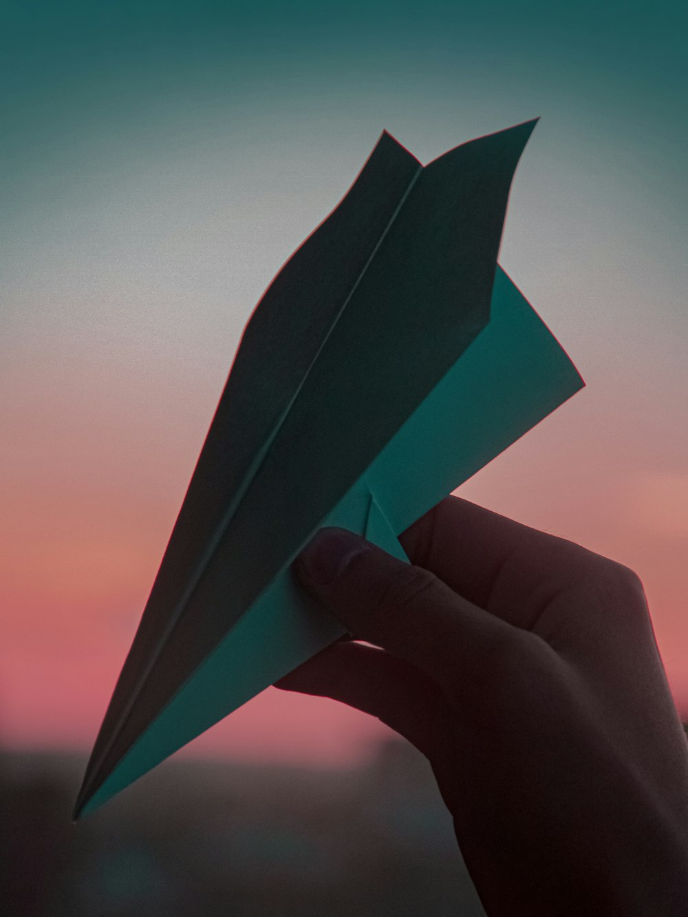 uma mão segurando um avião de papel na frente de um pôr do sol