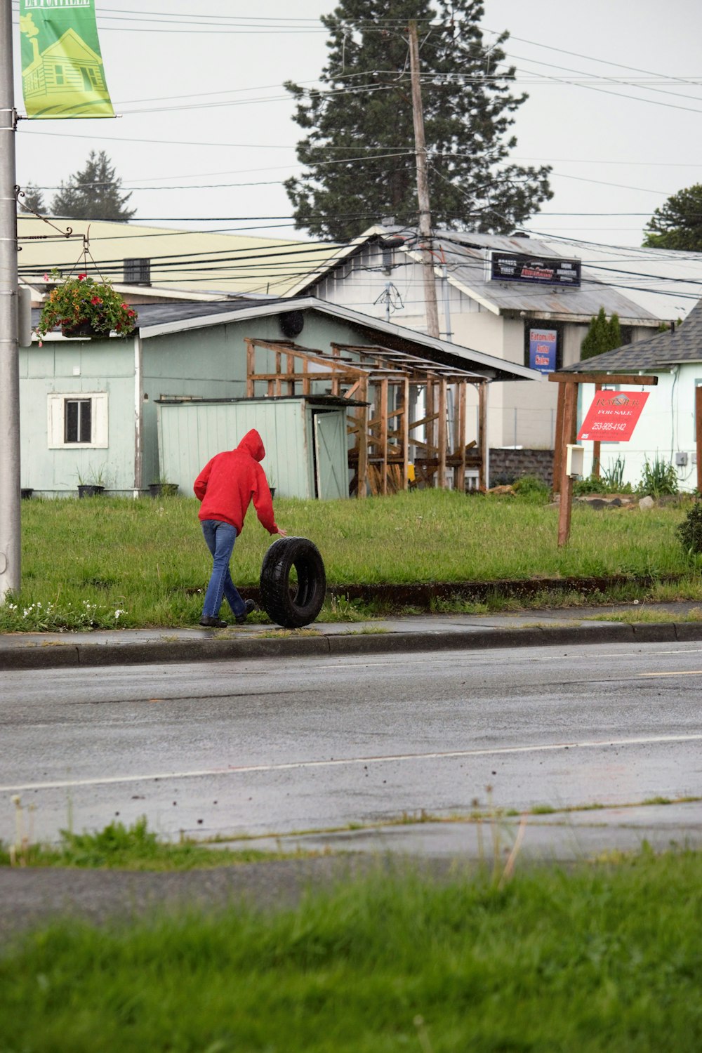 a person in a red jacket pushing a tire down a street