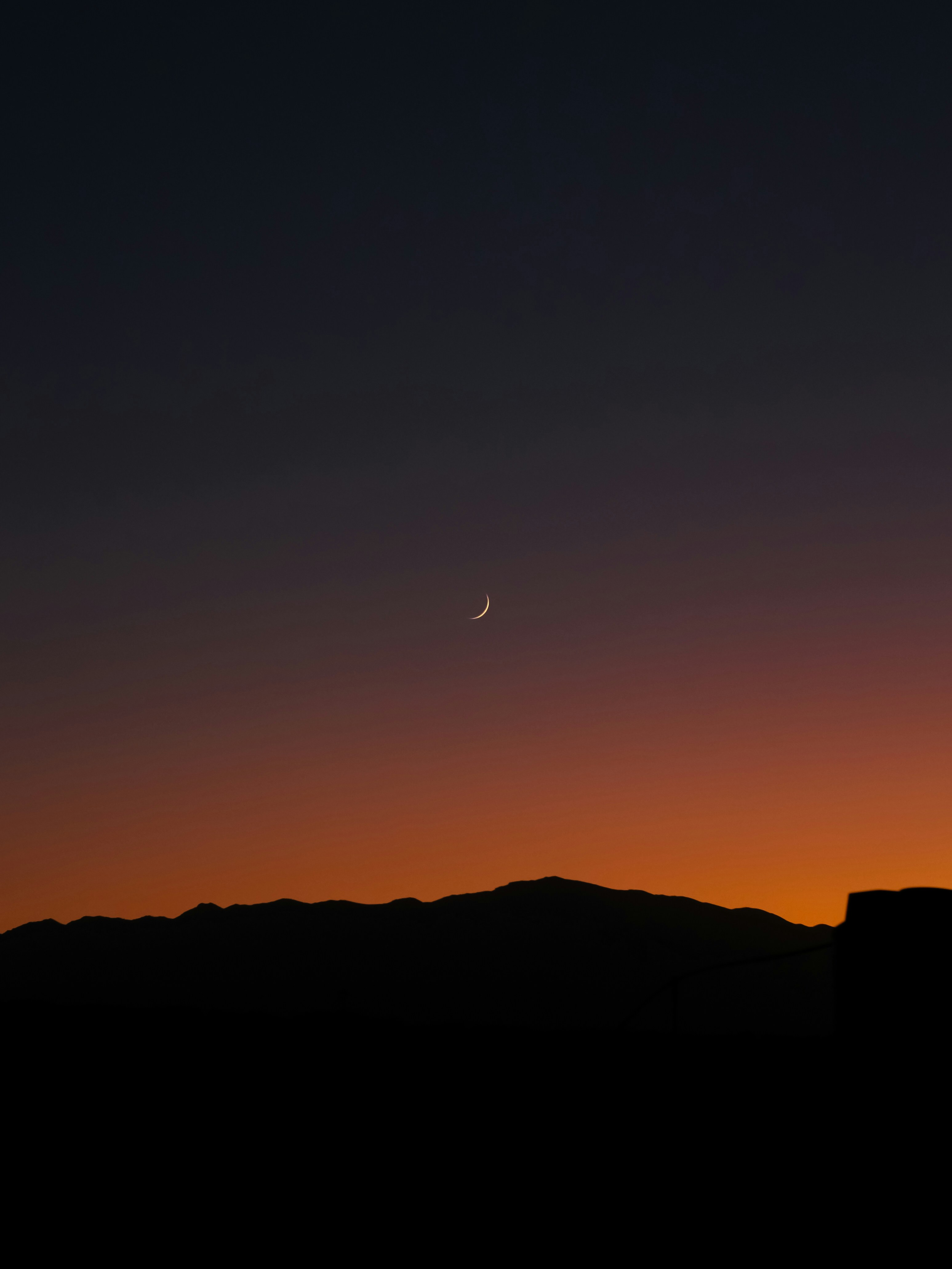 the moon is setting over a mountain range