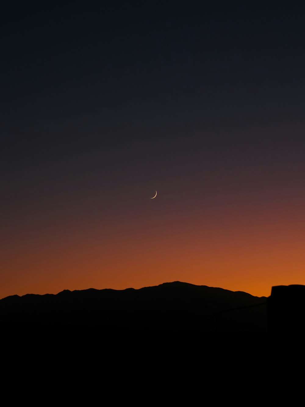 the moon is setting over a mountain range