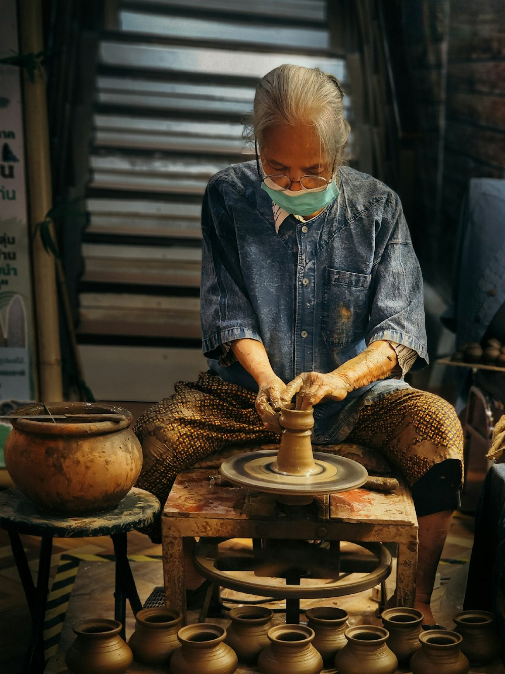 a man in a blue shirt and a mask working on a pottery wheel