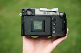 A compact point-and-shoot camera held in a hand with a bright outdoor setting.