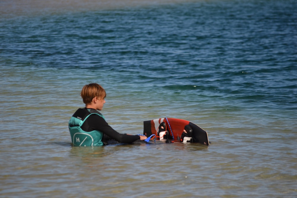 a young boy sitting in the water with a life jacket on