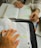 Two people are studying with books open on a table, one person has highlighted sections in orange and green. Their hands are visible, and there are notebooks and pens nearby.
