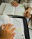 Two people are studying with books open on a table, one person has highlighted sections in orange and green. Their hands are visible, and there are notebooks and pens nearby.