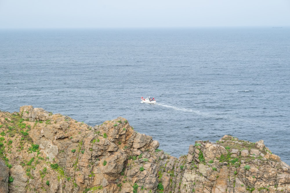 Una barca che viaggia sull'oceano vicino a una scogliera rocciosa