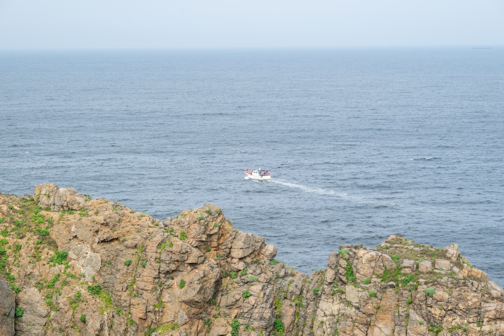 a boat traveling on the ocean near a rocky cliff