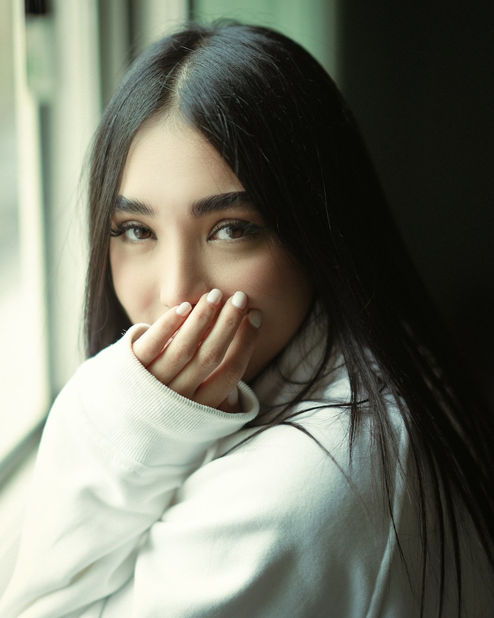 a woman with long black hair is looking out a window
