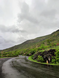 A winding mountain road with a taxi navigating carefully under cloudy skies.