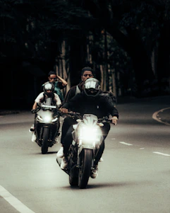 Dark-themed photo of a motorcycle group riding through a misty forest road at dusk