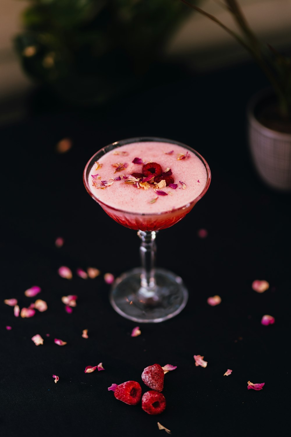 a small glass filled with a drink and garnished with rose petals