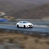 A white Porsche speeding along a coastal highway with ocean views.