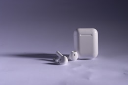 Wireless earbuds and their charging case are shown on a neutral background. The lighting highlights the sleek design and glossy finish of the devices.