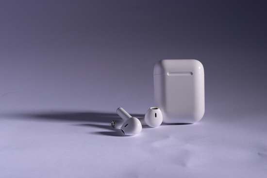 Wireless earbuds and their charging case are shown on a neutral background. The lighting highlights the sleek design and glossy finish of the devices.