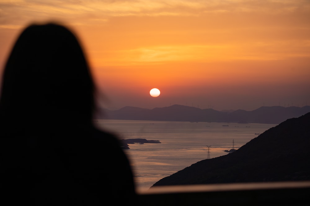 a woman looking at the sunset over a body of water