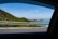 A friendly driver assisting passengers with their luggage near a scenic coastal road.
