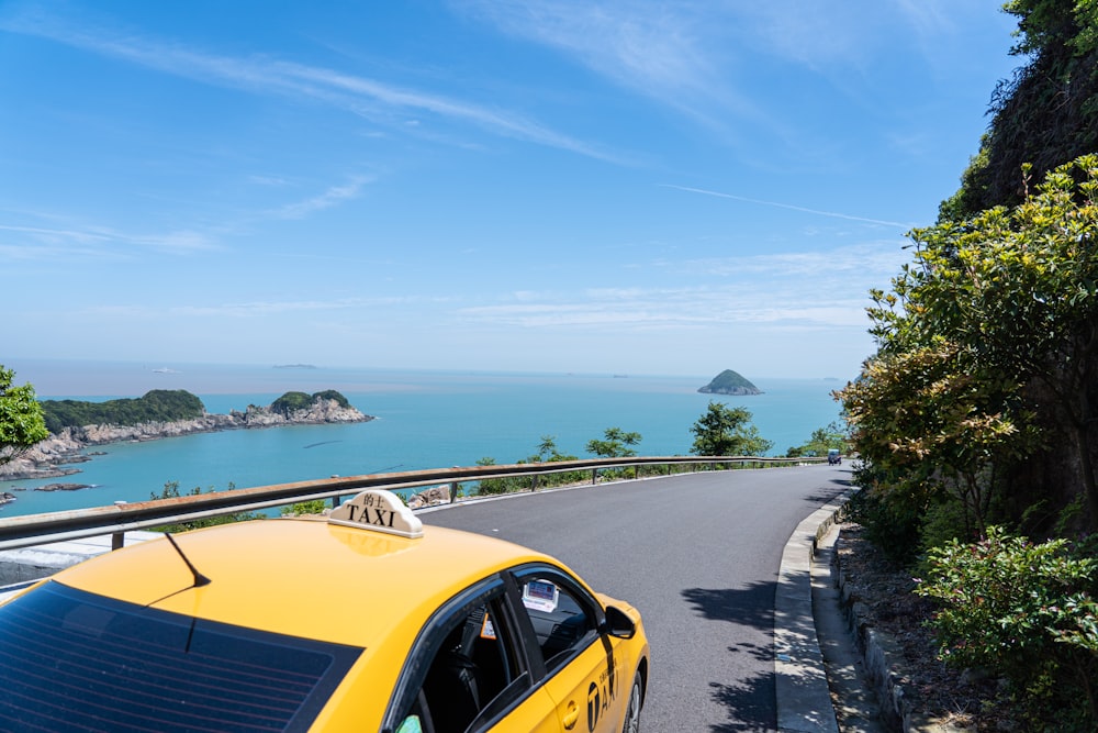 a yellow car driving down a road next to the ocean