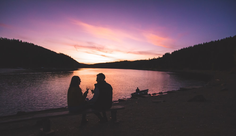 a man and a woman sitting on a bench next to a lake