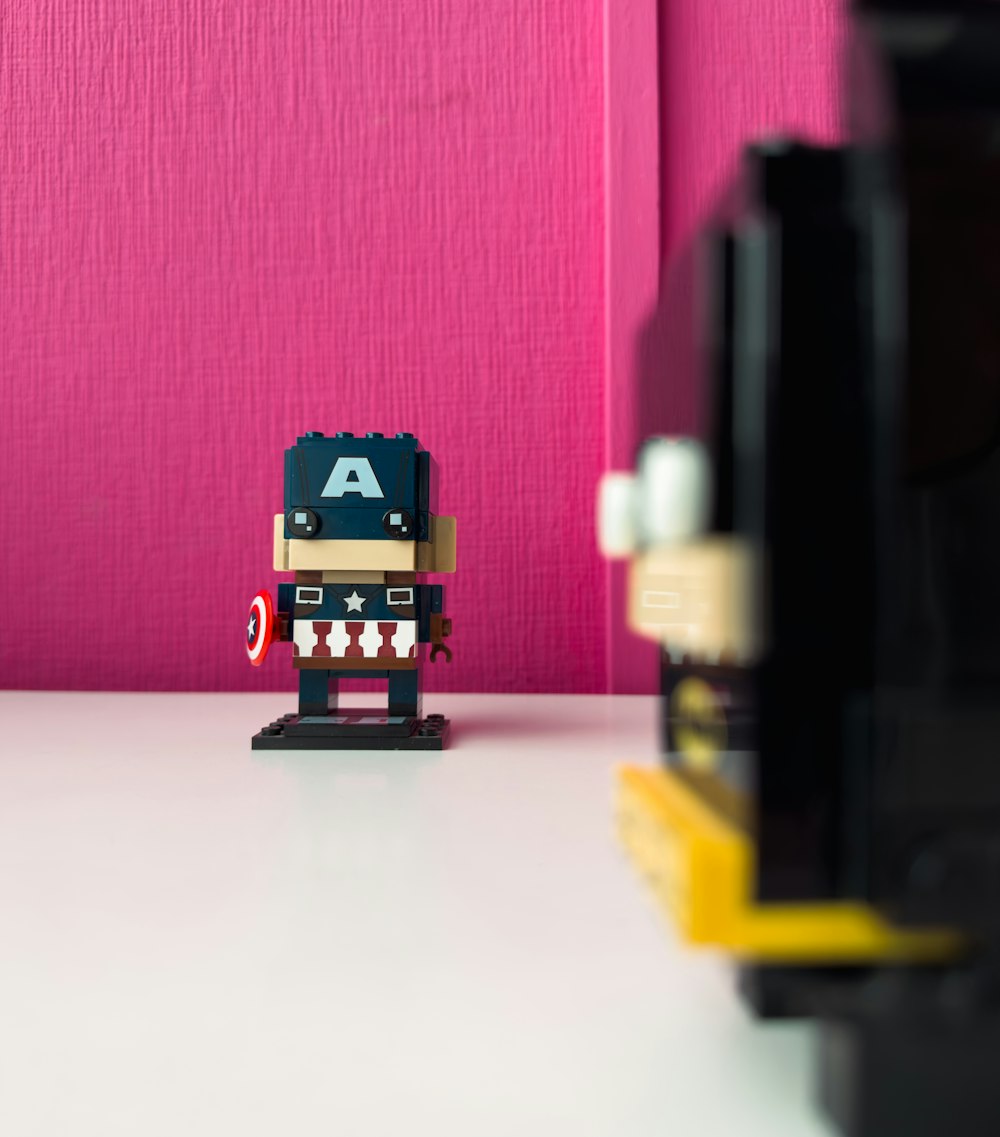 Eine Lego-Figur, die auf einem Tisch neben einer rosa Wand sitzt