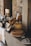 A rustic kitchen scene featuring various kitchen items on a counter next to a stone wall, including a freshly baked pie on a white ceramic tray, wooden utensils in a basket, candles, glassware, and ceramic jugs. The setting emphasizes a cozy and homely atmosphere with a vintage aesthetic.