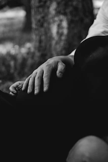 A close-up of gentle hands resting on a lap, surrounded by natural greenery in soft focus.