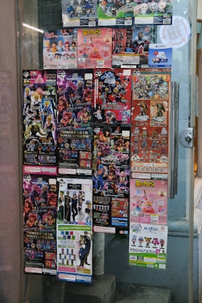 A window display covered with colorful posters featuring a variety of collectible figurines and merchandise. The posters depict animated characters and promotional images for toys, with text in different languages including Japanese. The items appear to be popular franchises, showcasing a vibrant and lively array of designs.