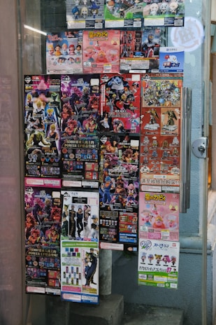 A window display covered with colorful posters featuring a variety of collectible figurines and merchandise. The posters depict animated characters and promotional images for toys, with text in different languages including Japanese. The items appear to be popular franchises, showcasing a vibrant and lively array of designs.