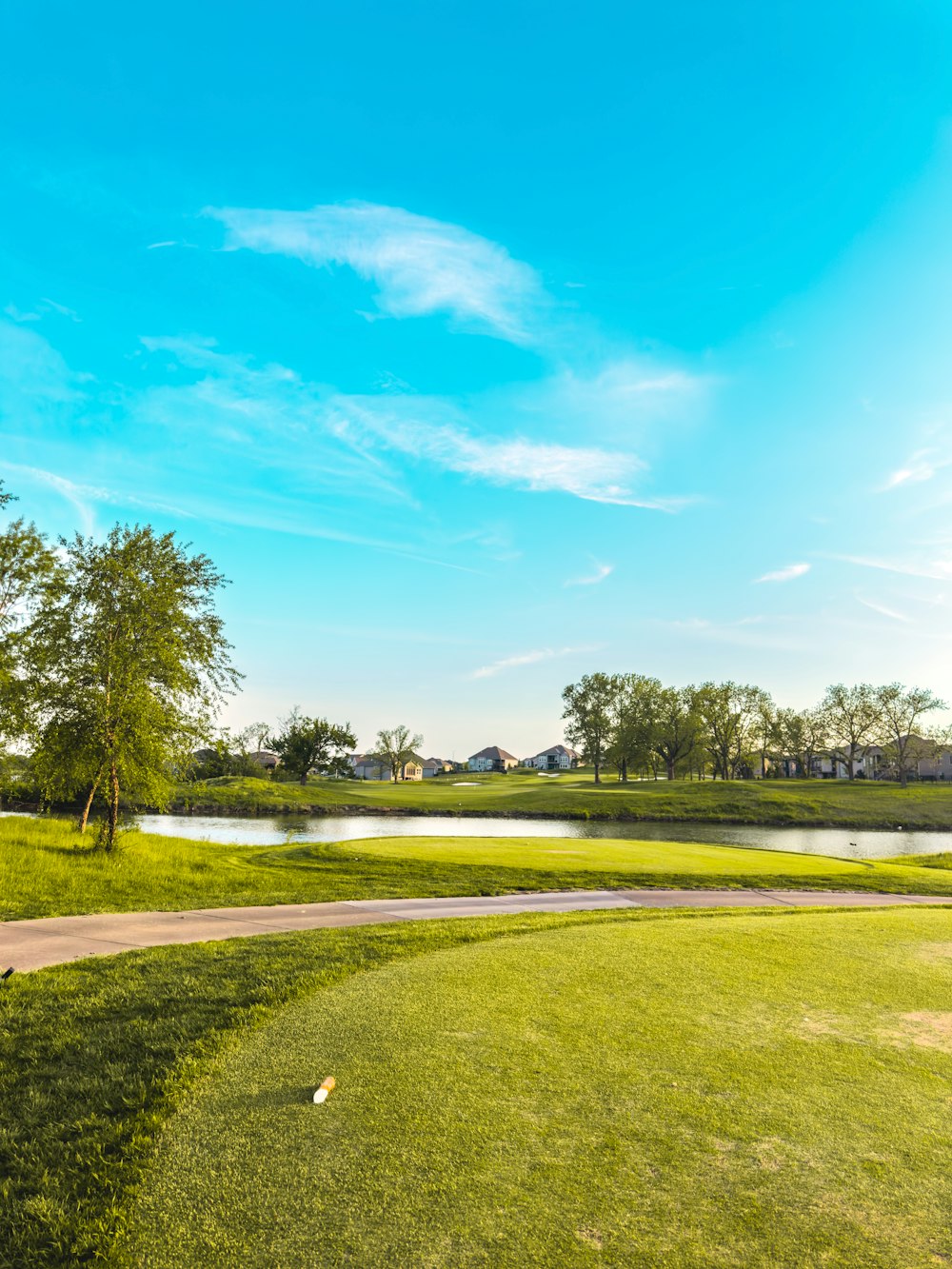 a green golf course with a pond and trees in the background