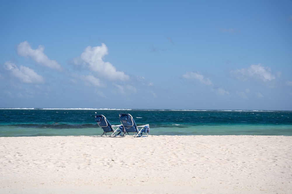 two lawn chairs sitting on top of a sandy beach