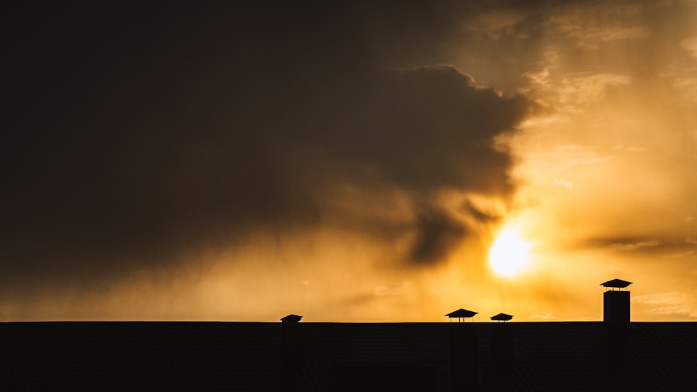 a group of birds sitting on top of a roof under a cloudy sky