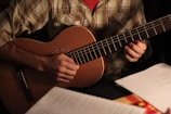 Hands playing an acoustic guitar surrounded by scattered sheet music.