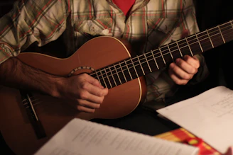 An overhead shot of hands playing an acoustic guitar with sheet music scattered nearby.
